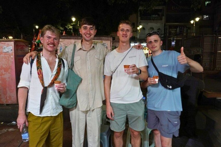 Four people standing outdoors at night, holding drinks, with a building and some lights in the background. 5