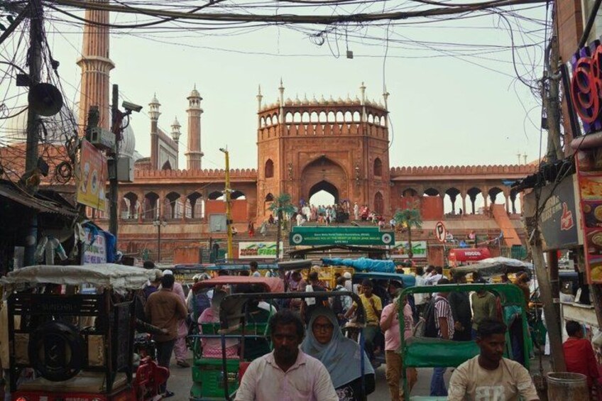 A busy street with a prominent historical building in the background, featuring a large archway and minarets. 2