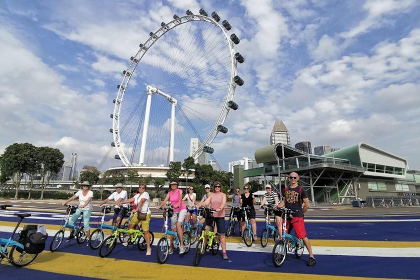 Un groupe de personnes à vélo devant une grande grande roue et des bâtiments modernes. 5