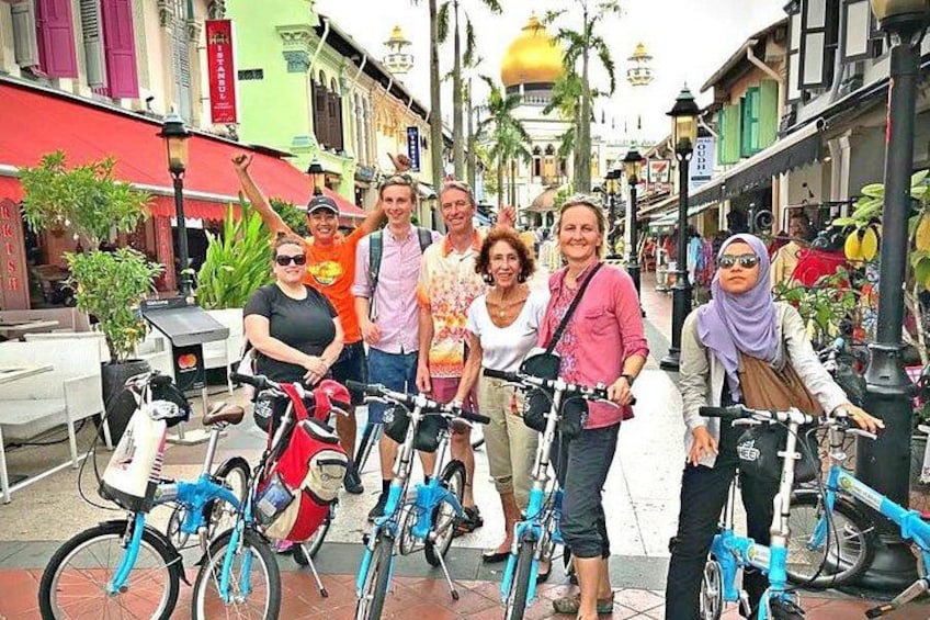 Un groupe de personnes posant avec des vélos dans une rue bordée de bâtiments colorés et de palmiers. 3