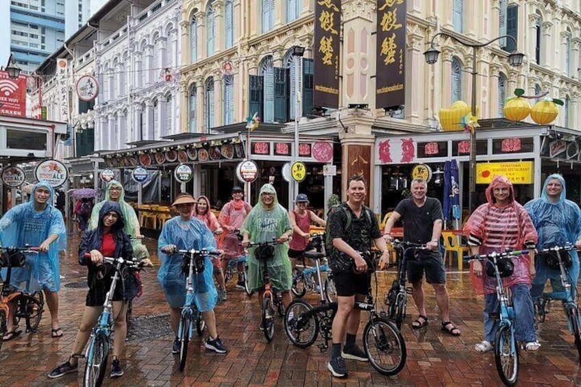 Een groep mensen op fietsen in een natte straat, met gebouwen op de achtergrond. 3