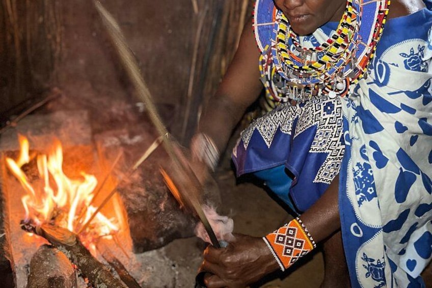 Eine Person kocht am offenen Feuer, gekleidet in traditioneller Tracht mit aufwendigen Mustern und Schmuck. 3