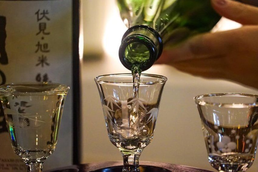 Una mano versa un liquido da una bottiglia verde in un bicchiere. 1