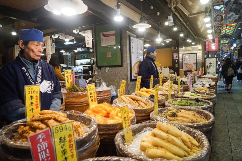A street market with various food stalls displaying items like fish, vegetables, and bread. 2