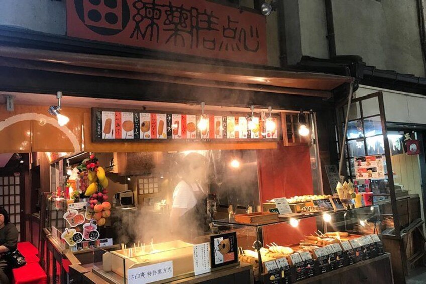A food stall with a variety of dishes displayed, a signboard with menu items, and a red awning. 2