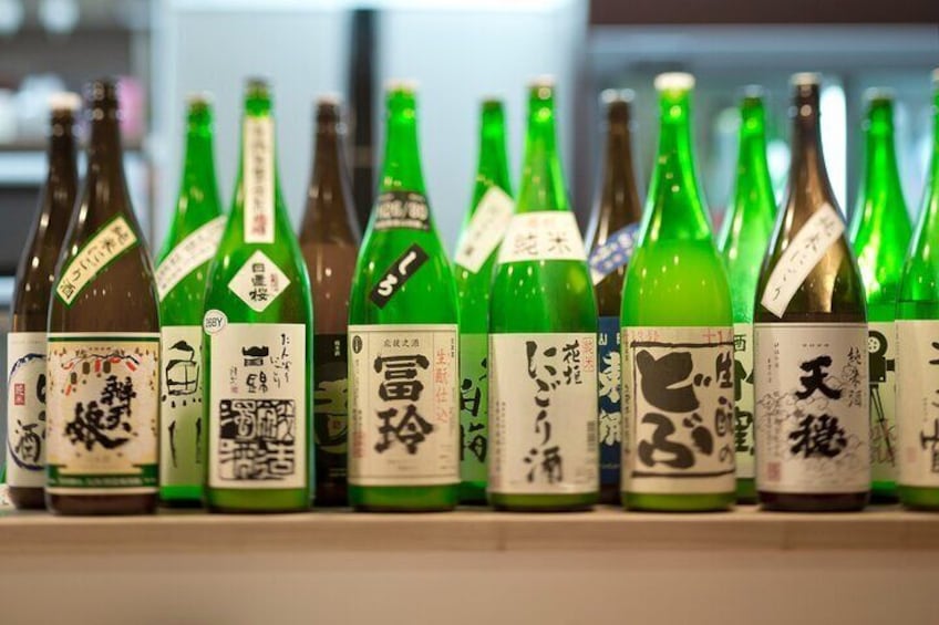 Botellas verdes en fila con etiquetas japonesas sobre una estantería. 3