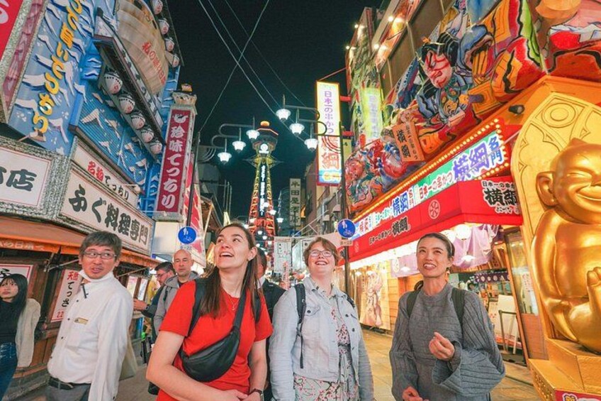 Una calle concurrida de noche, con carteles iluminados y una gran estatua dorada. 5