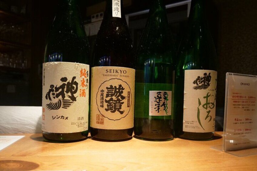 Cuatro botellas de sake con etiquetas, sobre una superficie de madera. 3