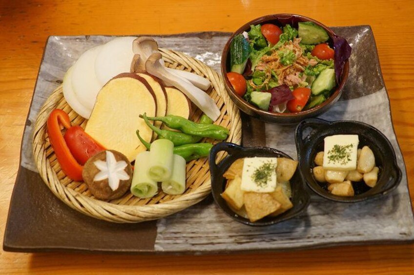 Une table en bois sur laquelle se trouve un repas composé de tranches de pain, d’une salade et de deux petits bols de fromage et de pommes de terre. 5