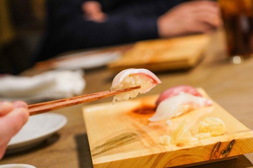 Une personne tenant des baguettes avec un morceau de sushi sur une planche en bois. 2