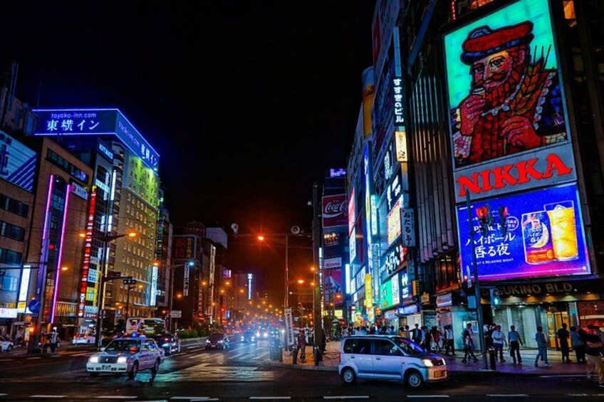Una strada cittadina luminosa di notte, con insegne al neon e pubblicità. 1