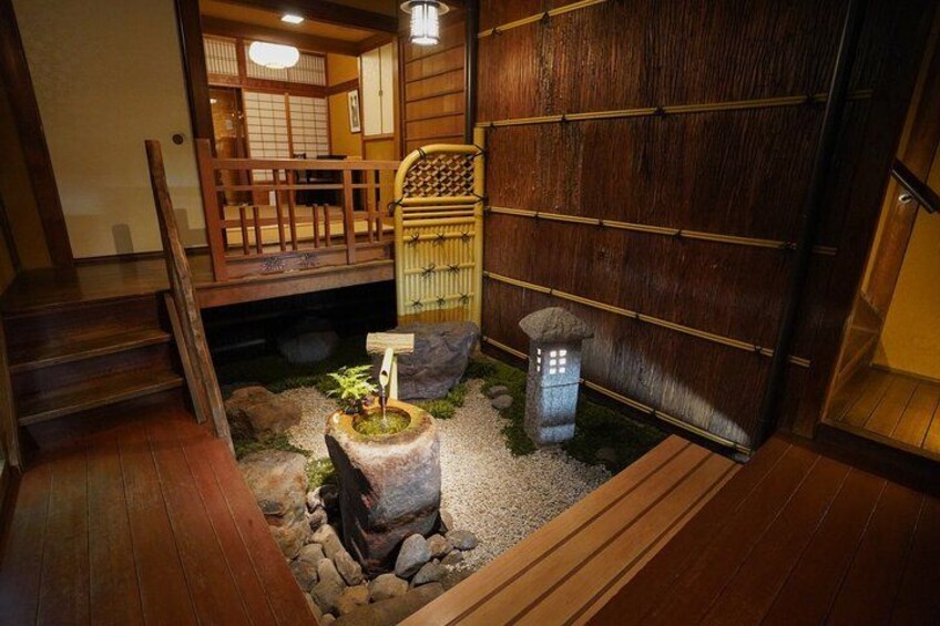 Een traditionele Japanse tuin met een houten trap, een stenen lantaarn en een klein waterpartij. 3