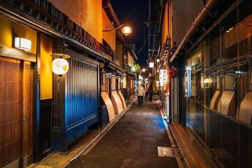 A narrow alleyway with traditional buildings, illuminated signs, and a person walking down the path. 5