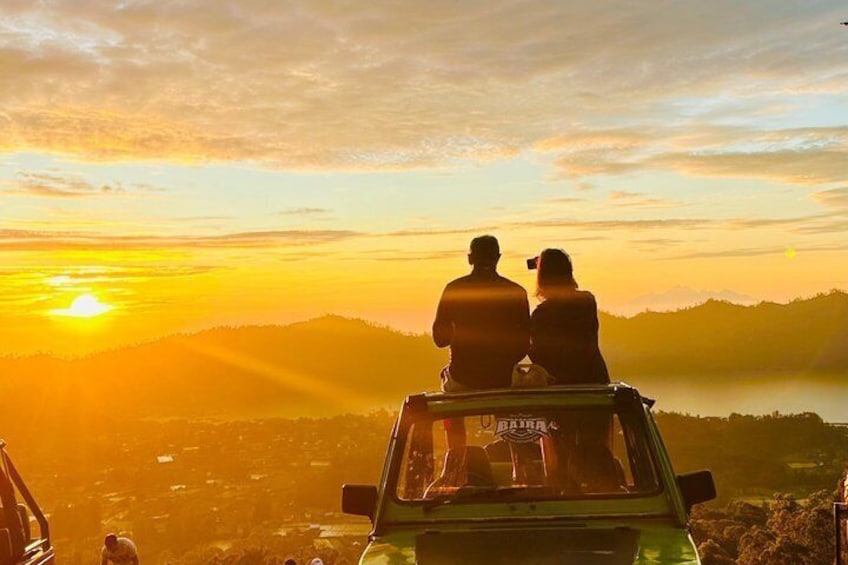 Zwei Personen sitzen in einem Fahrzeug, im Hintergrund ein Sonnenuntergang. 4