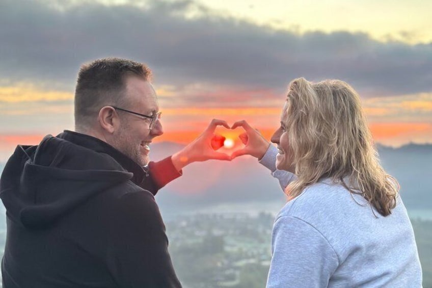 Zwei Personen formen mit ihren Händen ein Herz vor einem Sonnenuntergang. 5