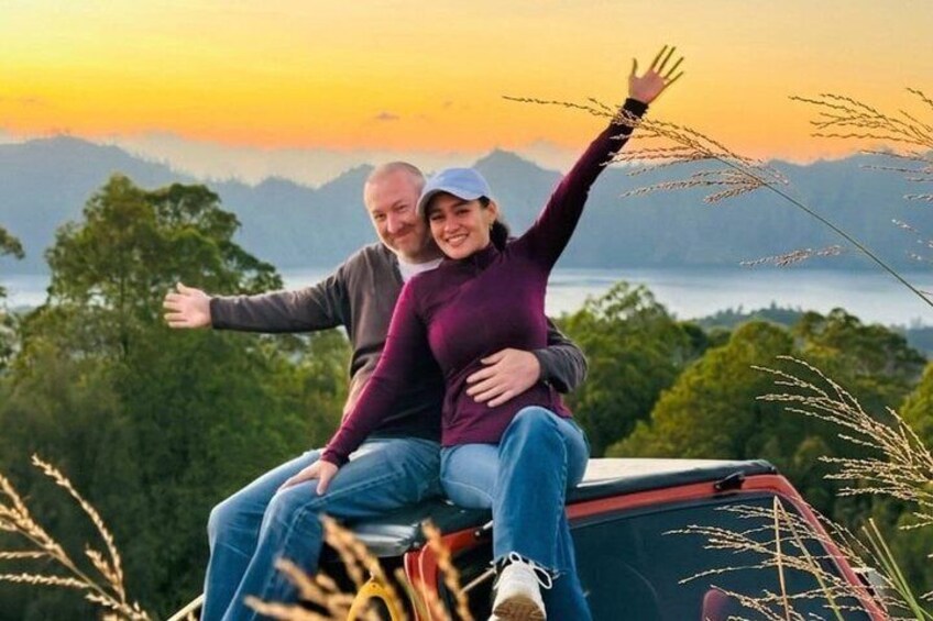 Zwei Personen sitzen in einem Fahrzeug mit Blick auf einen See und Berge im Hintergrund. 2