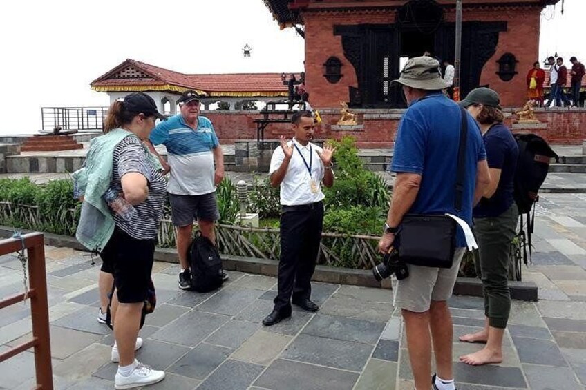 A group of tourists standing and conversing in front of a historical building with a red roof and black decorative elements. 3