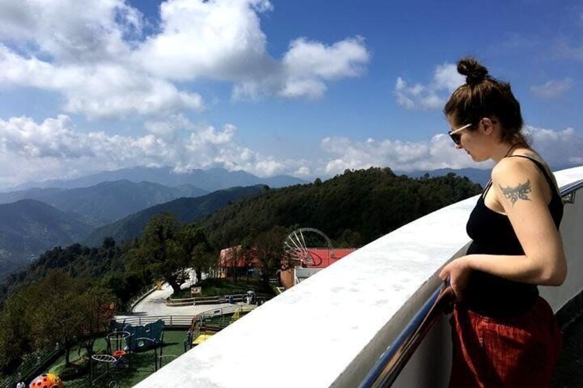 A person overlooking a mountainous landscape with a playground and buildings in the valley. 1