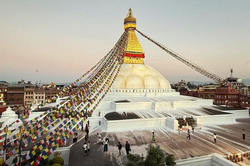 A large white stupa with a golden spire, surrounded by colorful prayer flags and people walking around. 5