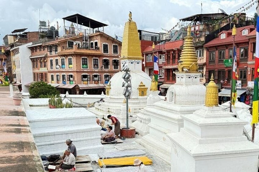 A white stupa with a golden spire, surrounded by buildings and flags. 3