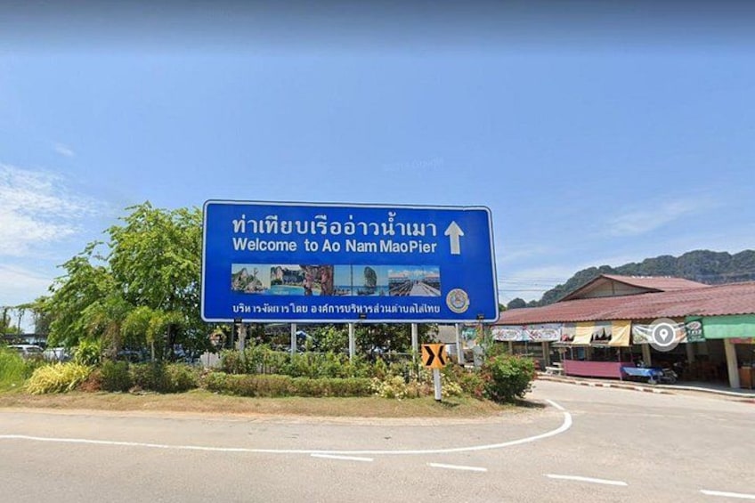 A road sign with a welcome message to Ao Nam Mao Pier, surrounded by greenery and a building with a red roof. 2