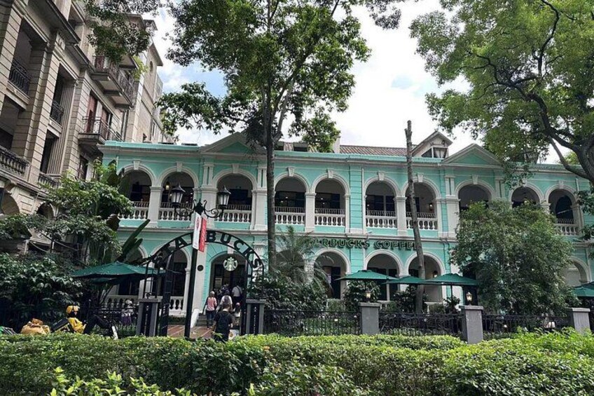 A historic building with arched windows and a green facade, surrounded by lush greenery and a fence. 5