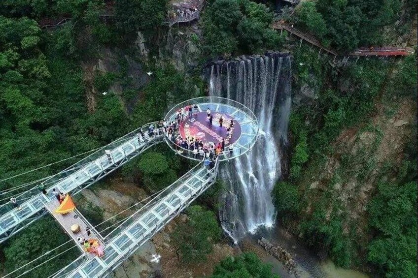 A glass bridge over a waterfall surrounded by dense forest. 2