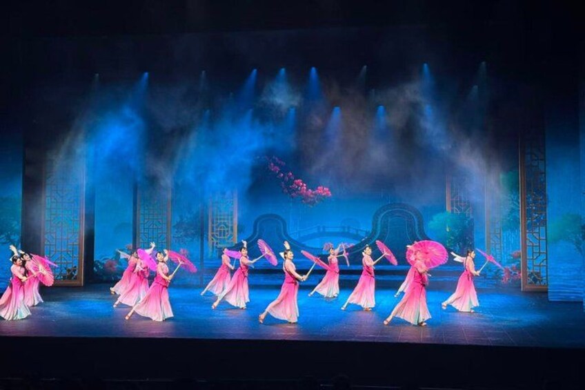 A stage with dancers in pink costumes performing a synchronized routine. 1