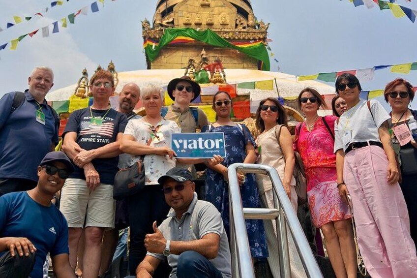 A group of people posing in front of a temple with a sign reading 'viator' and colorful flags. 1