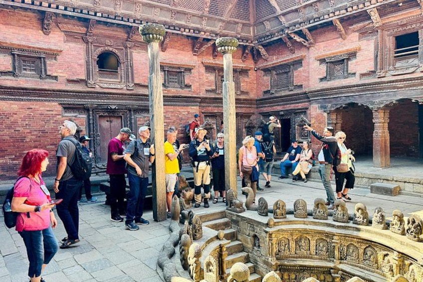 Un grupo de turistas explorando un antiguo patio con esculturas de piedra y una fuente. 4