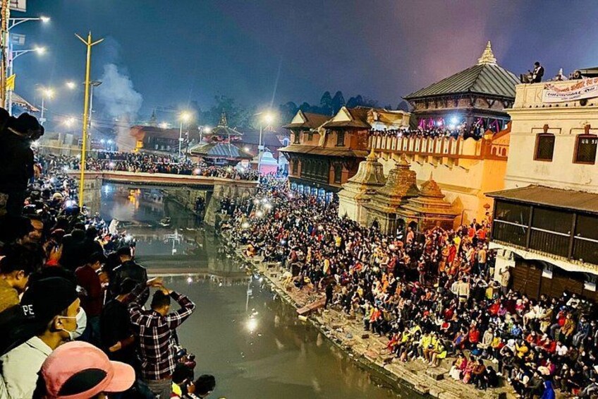 Un río concurrido, con gente reunida alrededor de un templo, un puente y edificios tradicionales. 2