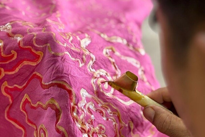 Una persona tiene un piccolo oggetto dorato vicino a un tessuto rosa con motivi elaborati. 3