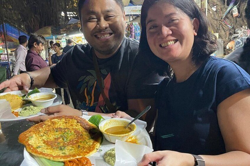 Two people sitting at a table with food, including a large flatbread and bowls of soup. 2