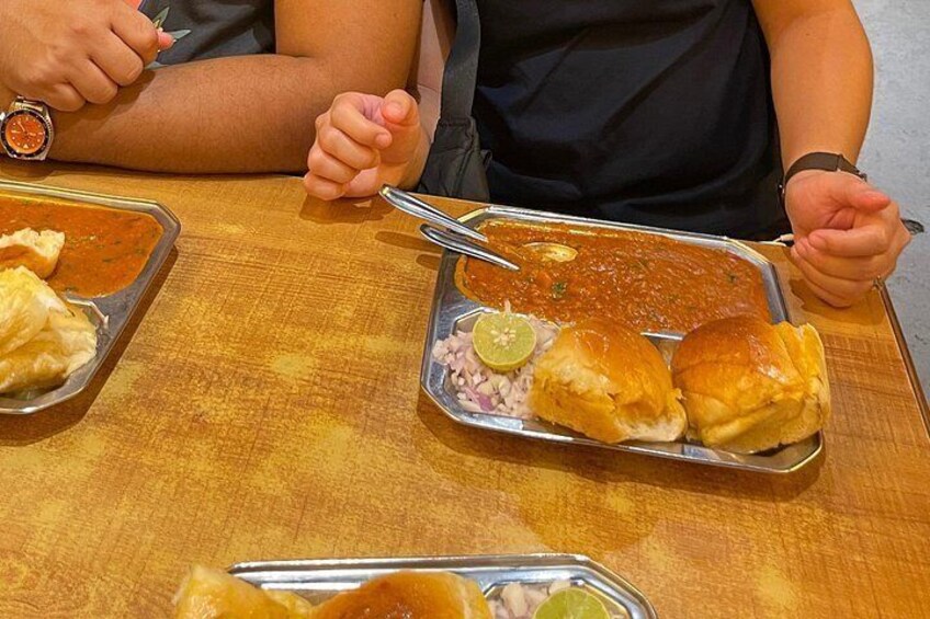 A meal with two metal plates, one containing a curry and the other containing bread rolls and a lime wedge. 4