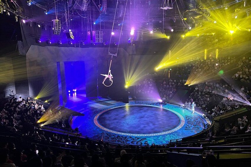 Eine große, überdachte Arena mit einer runden Bühne, Zuschauersitzen und Scheinwerfern. 3