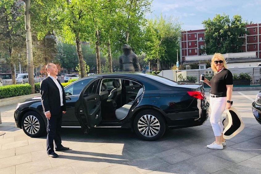 A black car parked on a paved area with trees and a statue in the background. 2