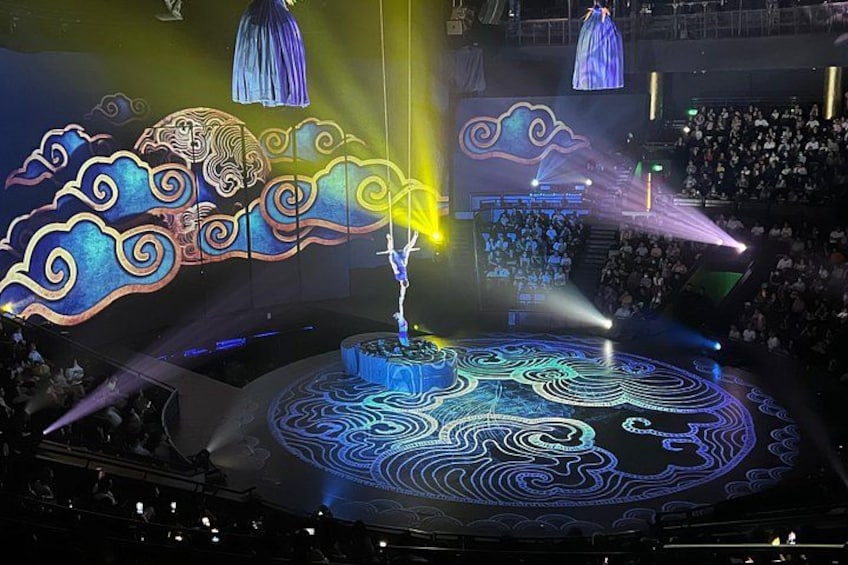 A stage with a blue and yellow light design, a large audience, and a performer in the center. 1