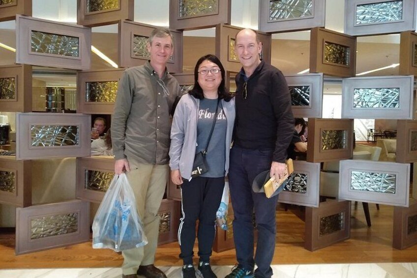 Three people standing in front of a wall with framed glass art. 5