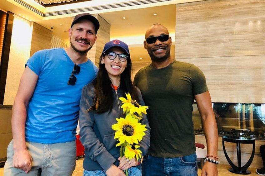 Three people standing indoors with a large window in the background. 3