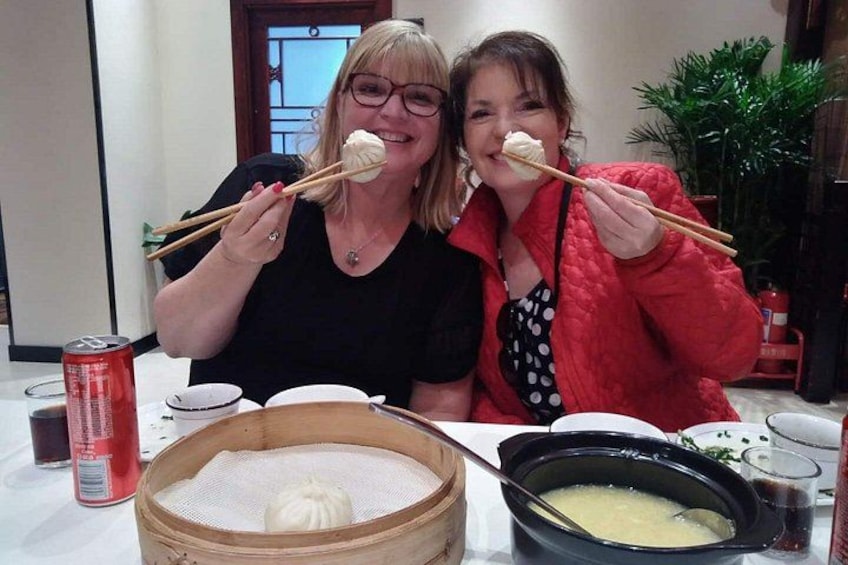 Two people holding chopsticks over a bowl of food, a can of soda, and a steaming pot on a table. 2