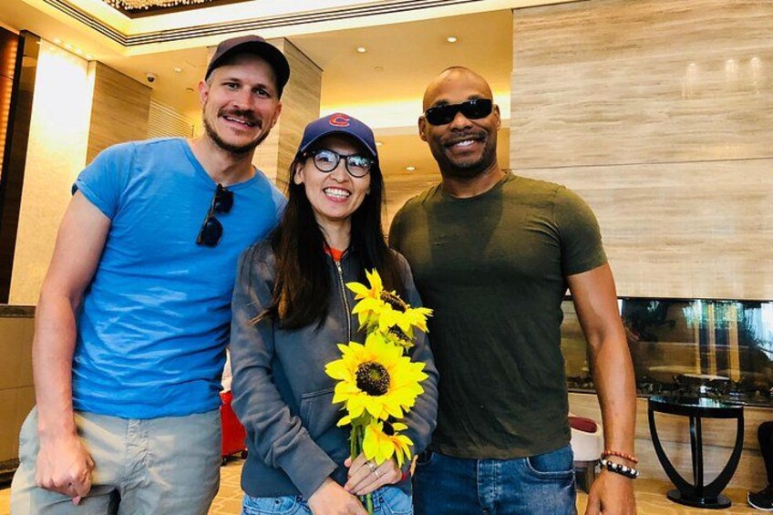 Three people standing indoors, one holding a sunflower. 2