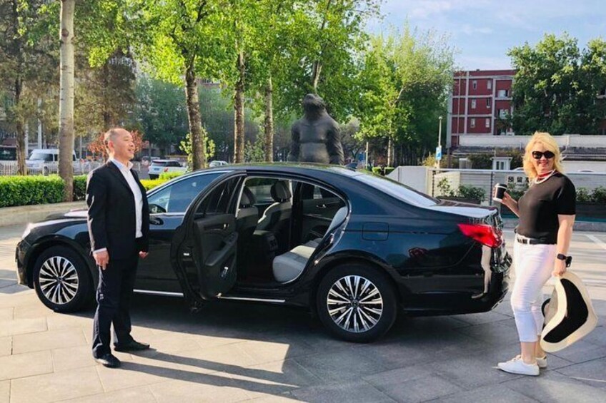 A black car parked on a paved area with trees and a statue in the background. 5