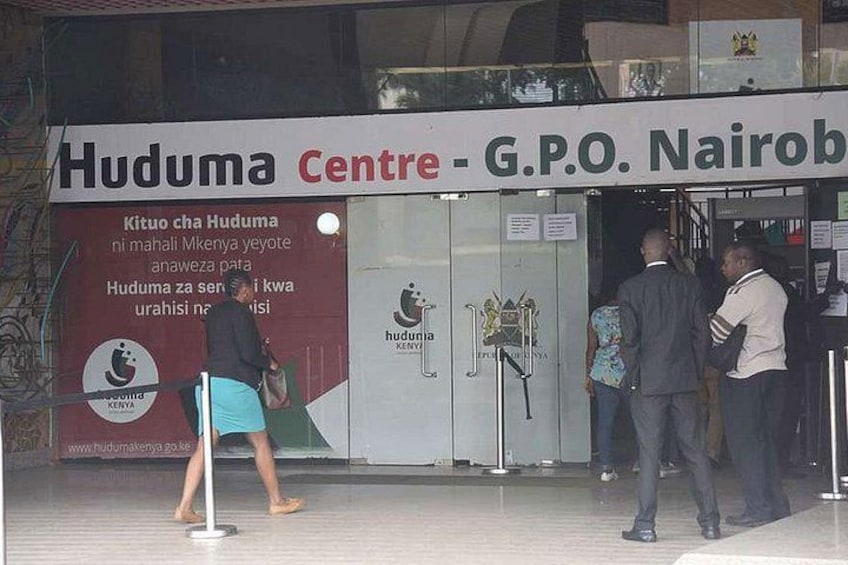 A Huduma Centre with a signboard, a woman walking, and two men standing. 1