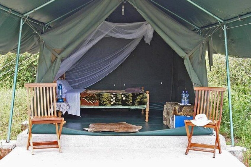 A tent with a bed, two chairs, and a table with water bottles. 1