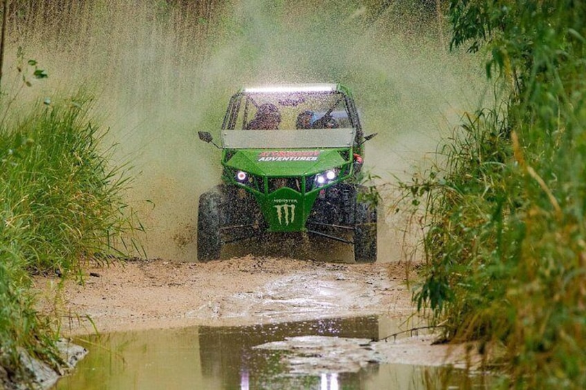 A green off-road vehicle driving through a muddy area with water puddles. 3