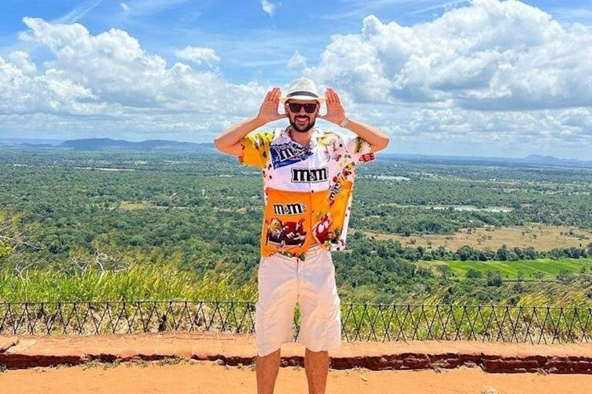 A person standing on a dirt path with a scenic view of a landscape with greenery and distant hills. 1