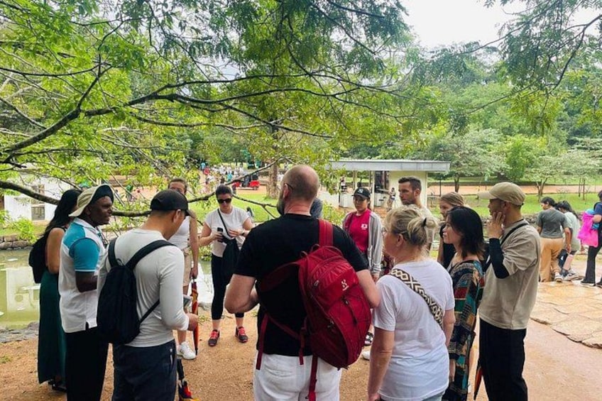 A group of people gathered outdoors, some with backpacks, under a tree canopy. 5