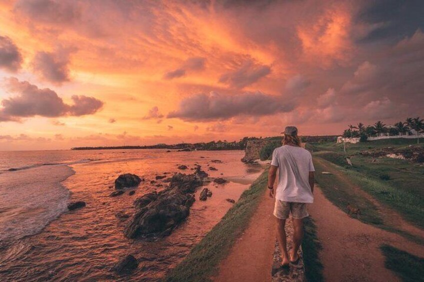 En person går på en sti ved siden af en strand i solnedgangen. 1