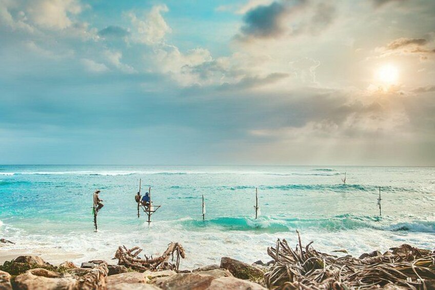 A beach with people standing on wooden structures in the water, a clear sky, and the ocean. 3