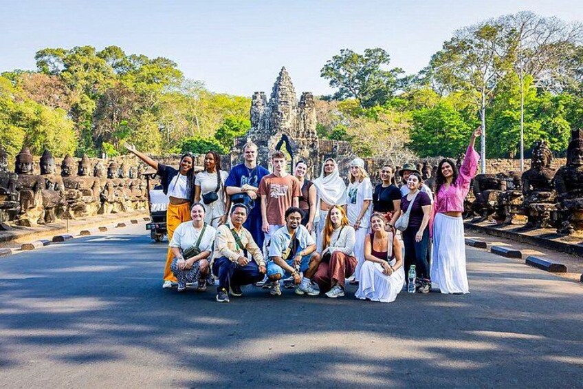 A group of people posing in front of a temple with stone statues and a large structure in the background. 3